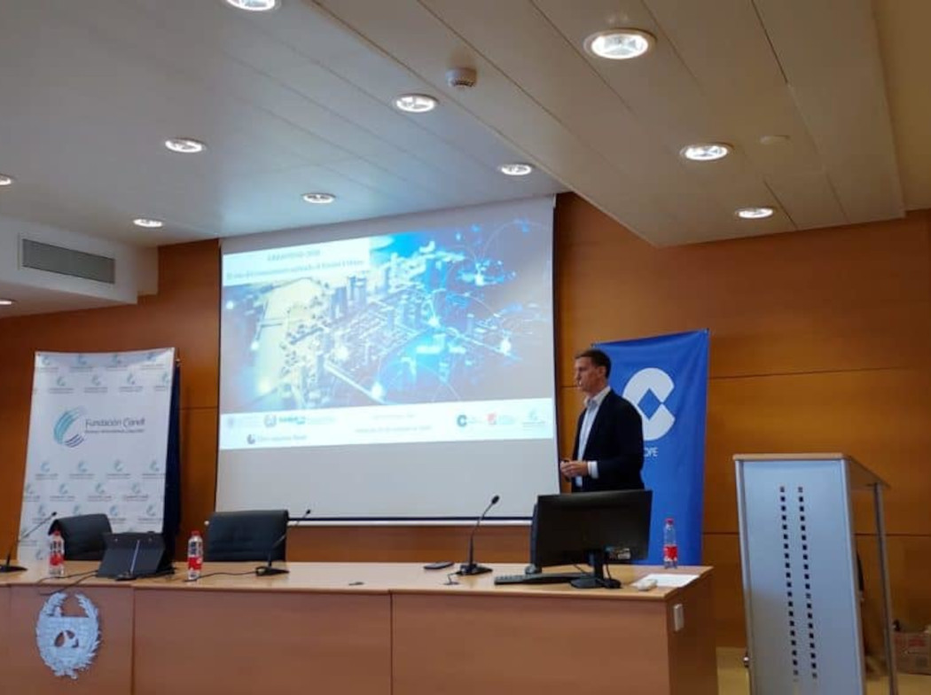 Sala de conferencias con el ponente Álvaro Moreno dirigiéndose a sentarse a la mesa