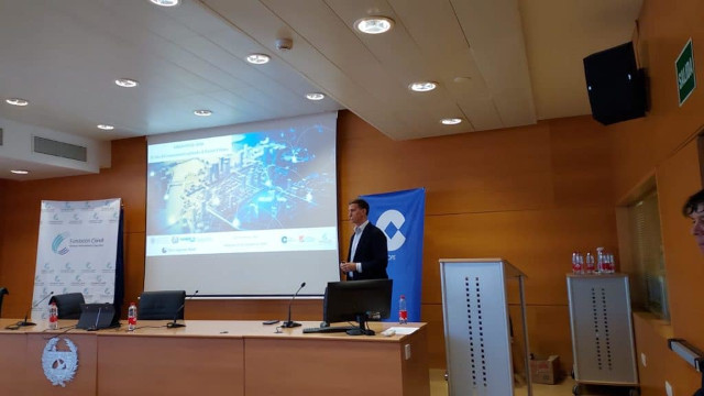 Sala de conferencias con el ponente Álvaro Moreno dirigiéndose a sentarse a la mesa
