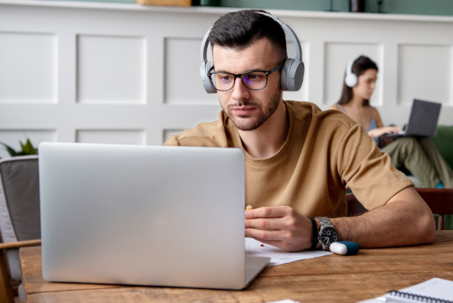 Hombre con auriculares puestos prestando atención a la pantallas del ordenador portátil