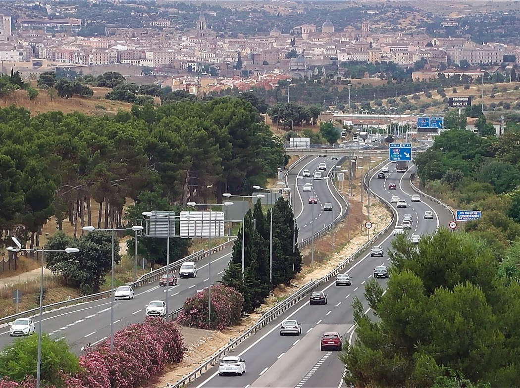 Vista aérea de una carretera de acceso a una ciudad con dos carriles por sentido, tráfico denso de vehículos y árboles alineados a los lados Vista aérea de una carretera de acceso a una ciudad con dos carriles por sentido, tráfico denso de vehículos y árboles alineados a los lados