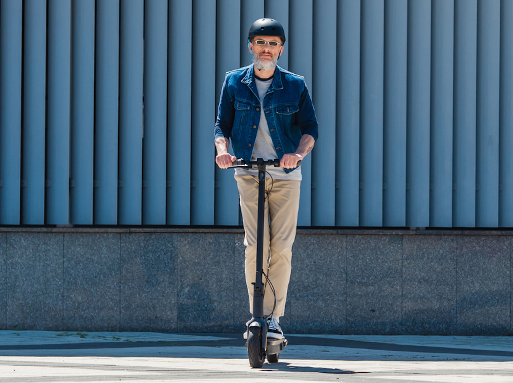 Hombre con casco y gafas de sol montado sobre un patinete eléctrico