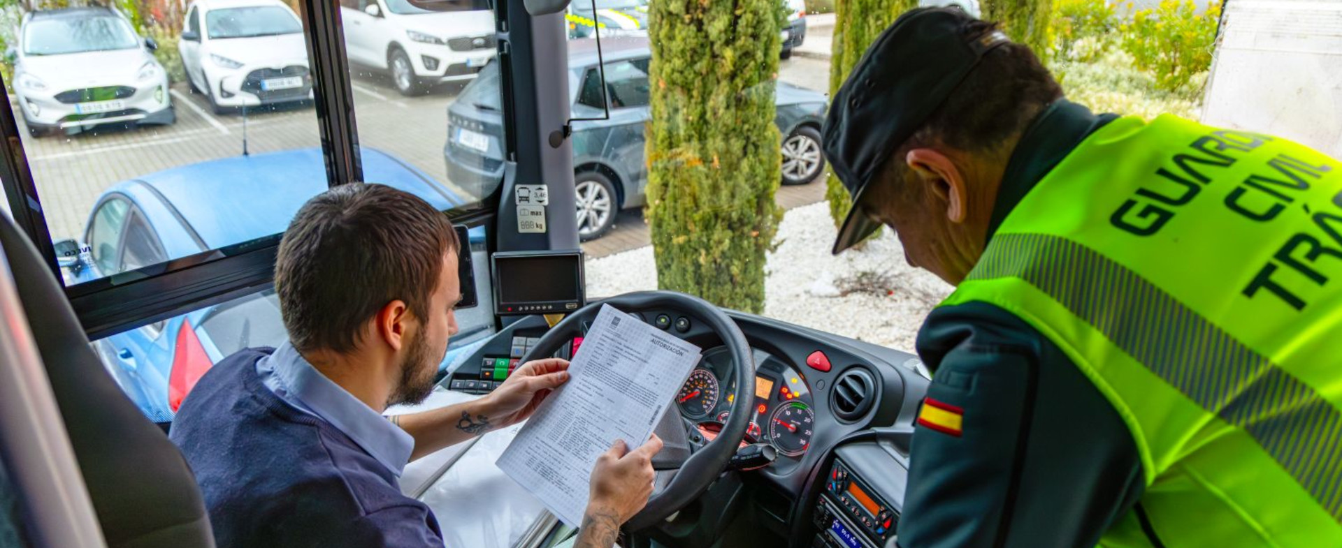 Un conductor de autobús sentado en el asiento del conductor con un papel entre sus manos y un guardia civil de pie a su lado en el interior de un autobús