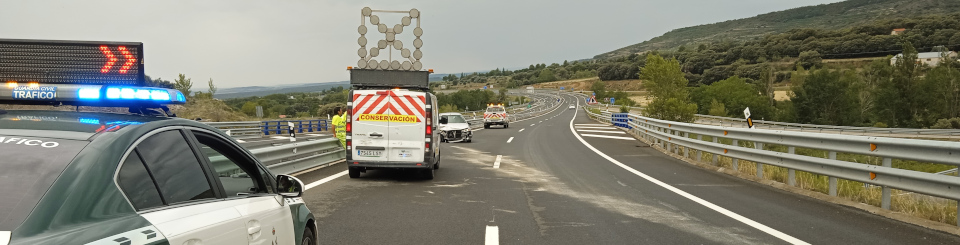 Carretera con curvas. A la izquierda, un coche de la Guardia Civil de Tráfico detenido. Al fondo, una furgoneta de Conservación de Carreteras está situada frente a un coche accidentado