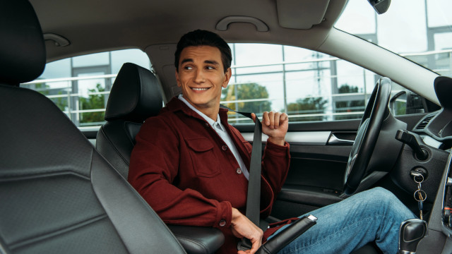 Hombre sentado en el interior de un coche abrochándose el cinturón de seguridad