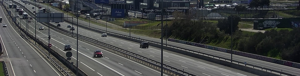 Autovía con tráfico de coches y camiones, con pabellones empresariales al fondo