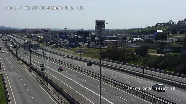 Autovía con tráfico de coches y camiones, con pabellones empresariales al fondo