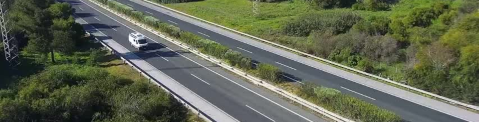 Imagen de una autovía en la que circulan un cocho y un camión, rodeada de vegetación.