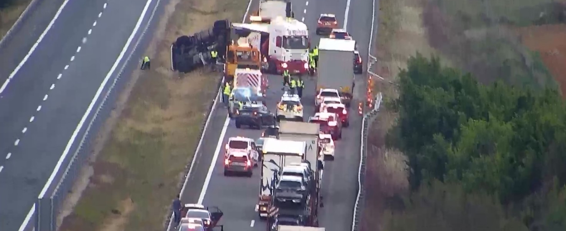 Imagen de un accidente en una autopista donde se ve un coche volcado en el arcén y varios coches y camiones parados.