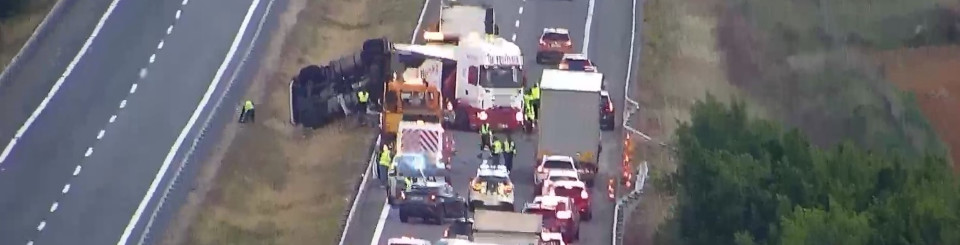 Imagen de un accidente en una autopista donde se ve un coche volcado en el arcén y varios coches y camiones parados.