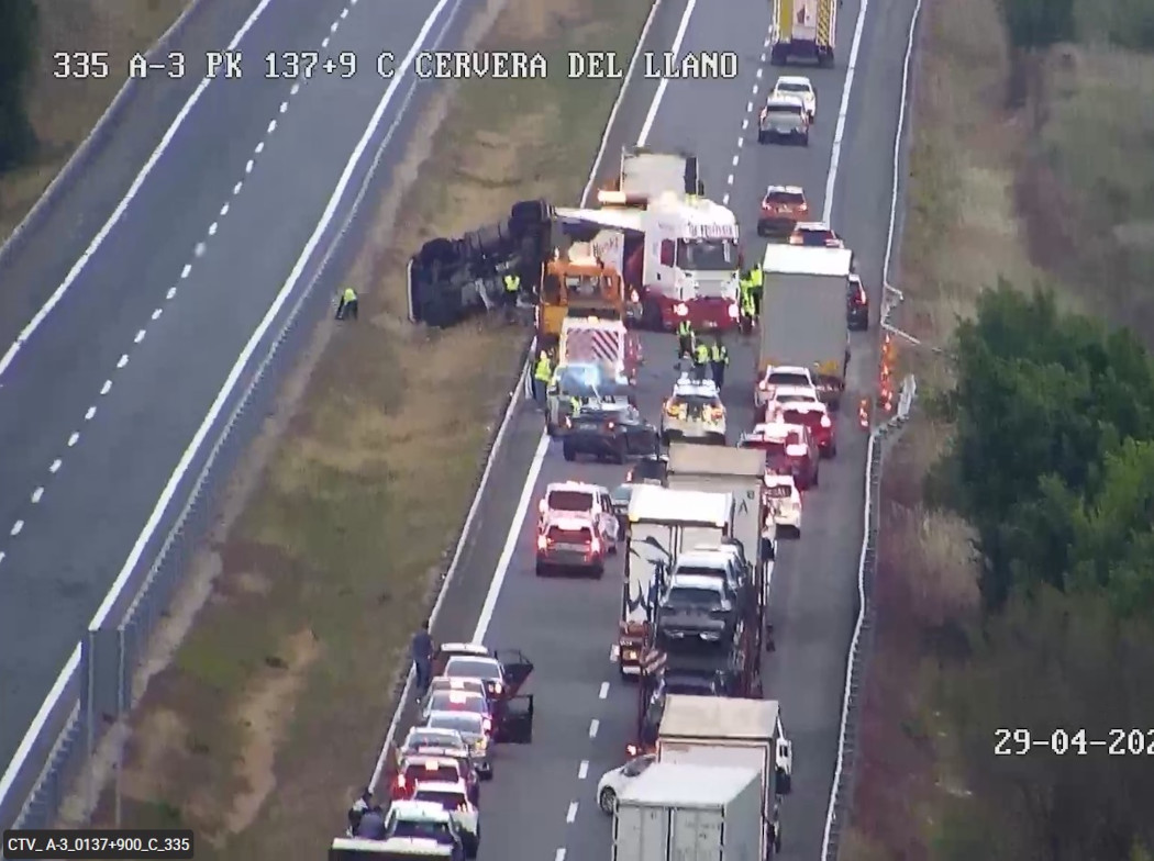 Imagen de un accidente en una autopista donde se ve un coche volcado en el arcén y varios coches y camiones parados.
