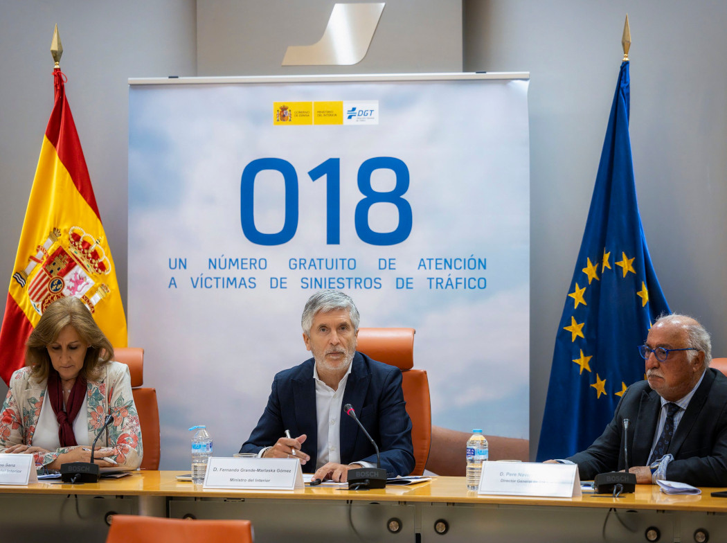 Grande-Marlaska, Pere Navarro y en una rueda de prensa sentados. Detrás de ellos, está un cartel con los números 018 en grande y las banderas de España y de la Unión Europea a los lados.