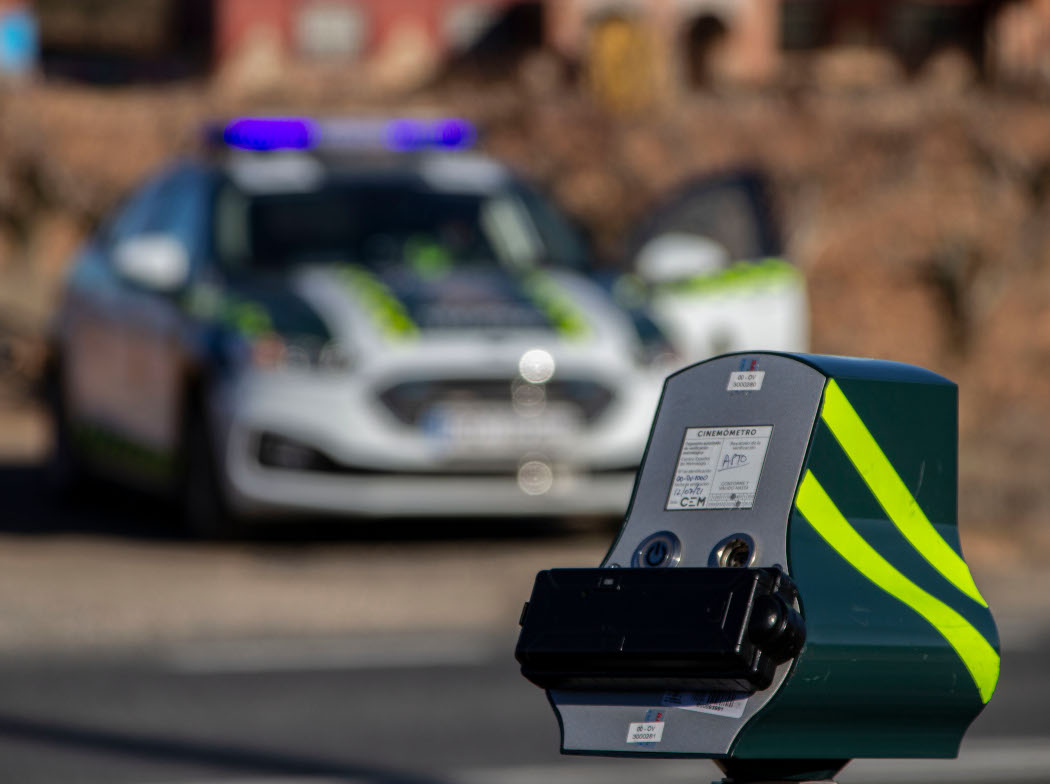 Veloláser en primer plano con un coche de la Guardia Civil desenfocado al fondo