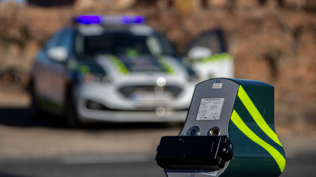 Veloláser en primer plano con un coche de la Guardia Civil desenfocado al fondo