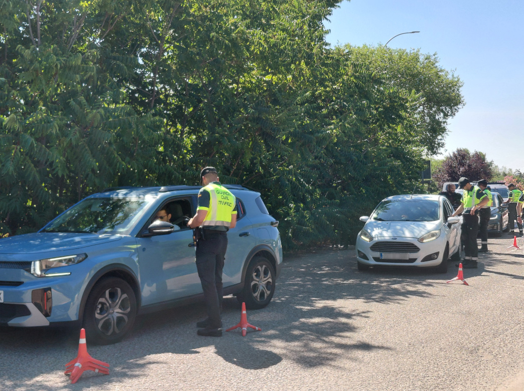 Un grupo de guardias civiles realiza un control de alcohol y drogas a los conductores de varios coches detenidos en una carretera, junto a una arboleda