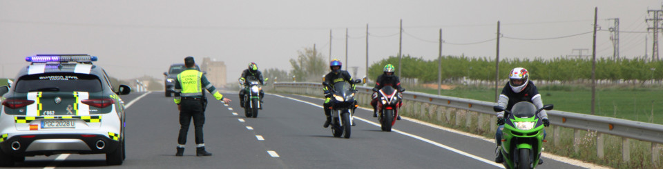 Carretera con motociclistas circulando y vigilada por una patrulla de la Guardia Civil