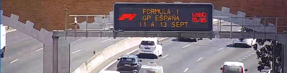 Vía de cuatro carriles con mucho tráfico y un panel informativo de tráfico sobre la calzada.