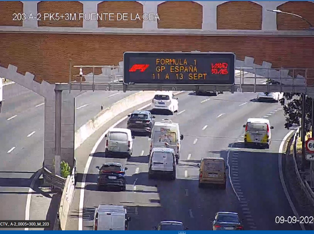 Vía de cuatro carriles con mucho tráfico y un panel informativo de tráfico sobre la calzada.