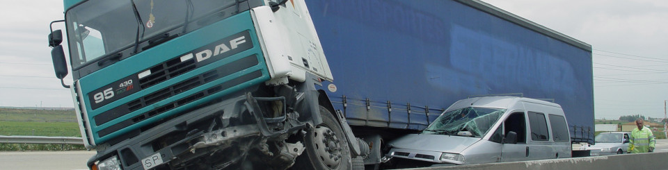 Camión accidentado sobre la barrera de una carretera, aplastando una furgoneta gris.