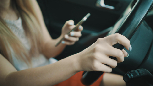 Mujer mirando el móvil en una mano y la otra puesta en el volante de un coche.