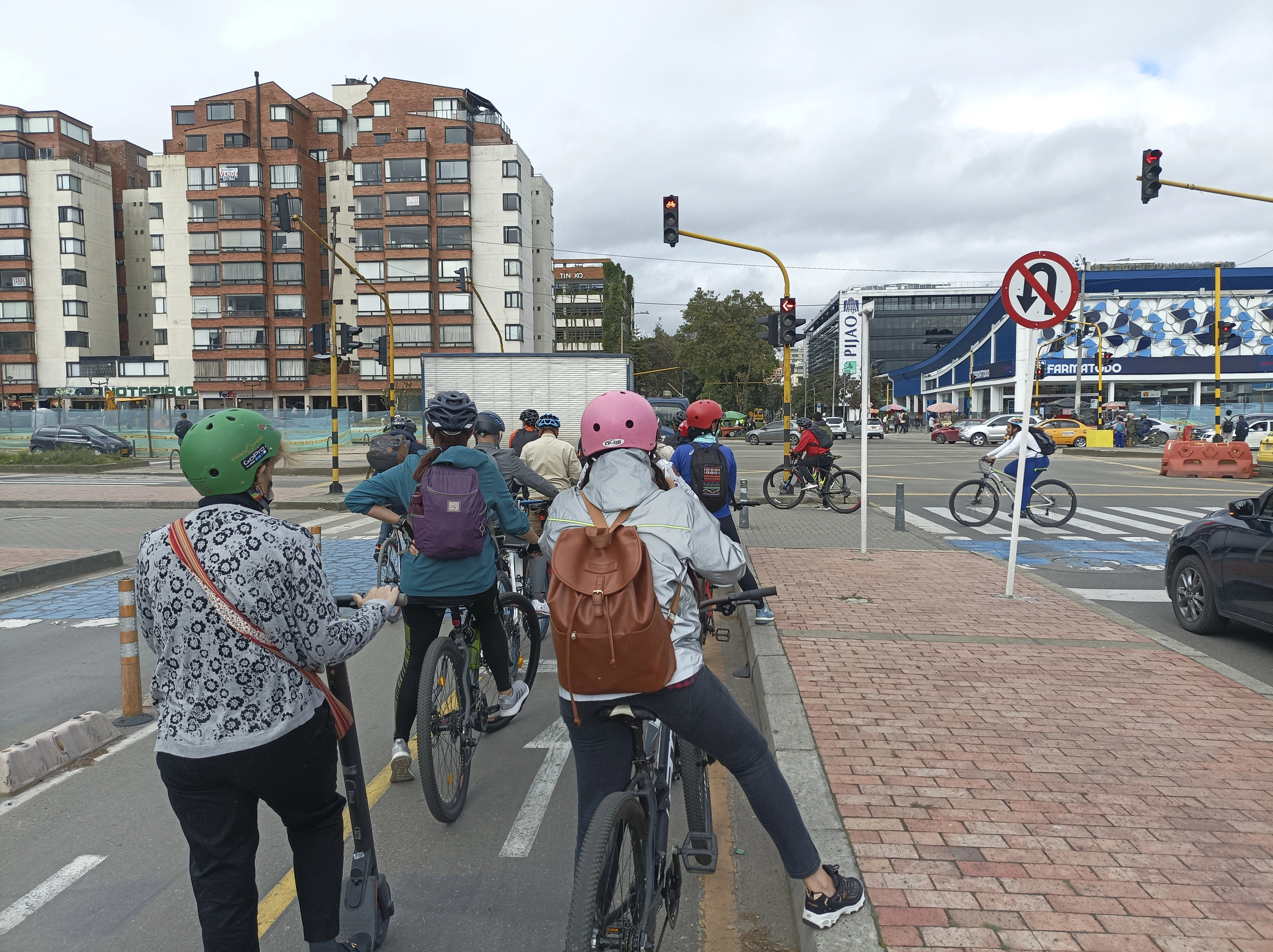 Imagen de una carretera de ciudad con varios ciclistas en línea parados en un semáforo en rojo. 
