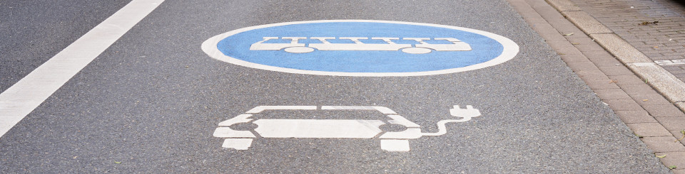 Imagen de un carril de carretera de asfalto con los icono pintados en blanco de una bicicleta, un coche eléctrico y autobús