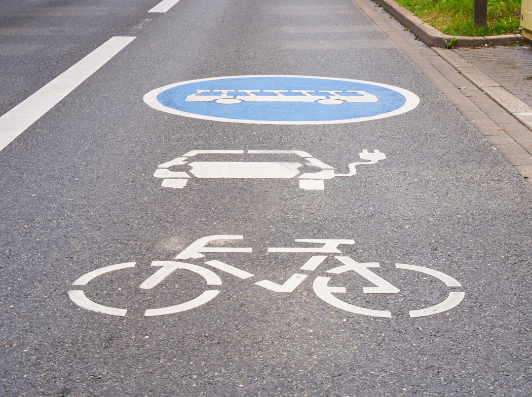 Imagen de un carril de carretera de asfalto con los icono pintados en blanco de una bicicleta, un coche eléctrico y autobús.