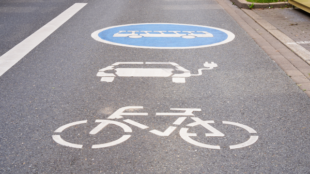 Imagen de un carril de carretera de asfalto con los icono pintados en blanco de una bicicleta, un coche eléctrico y autobús.