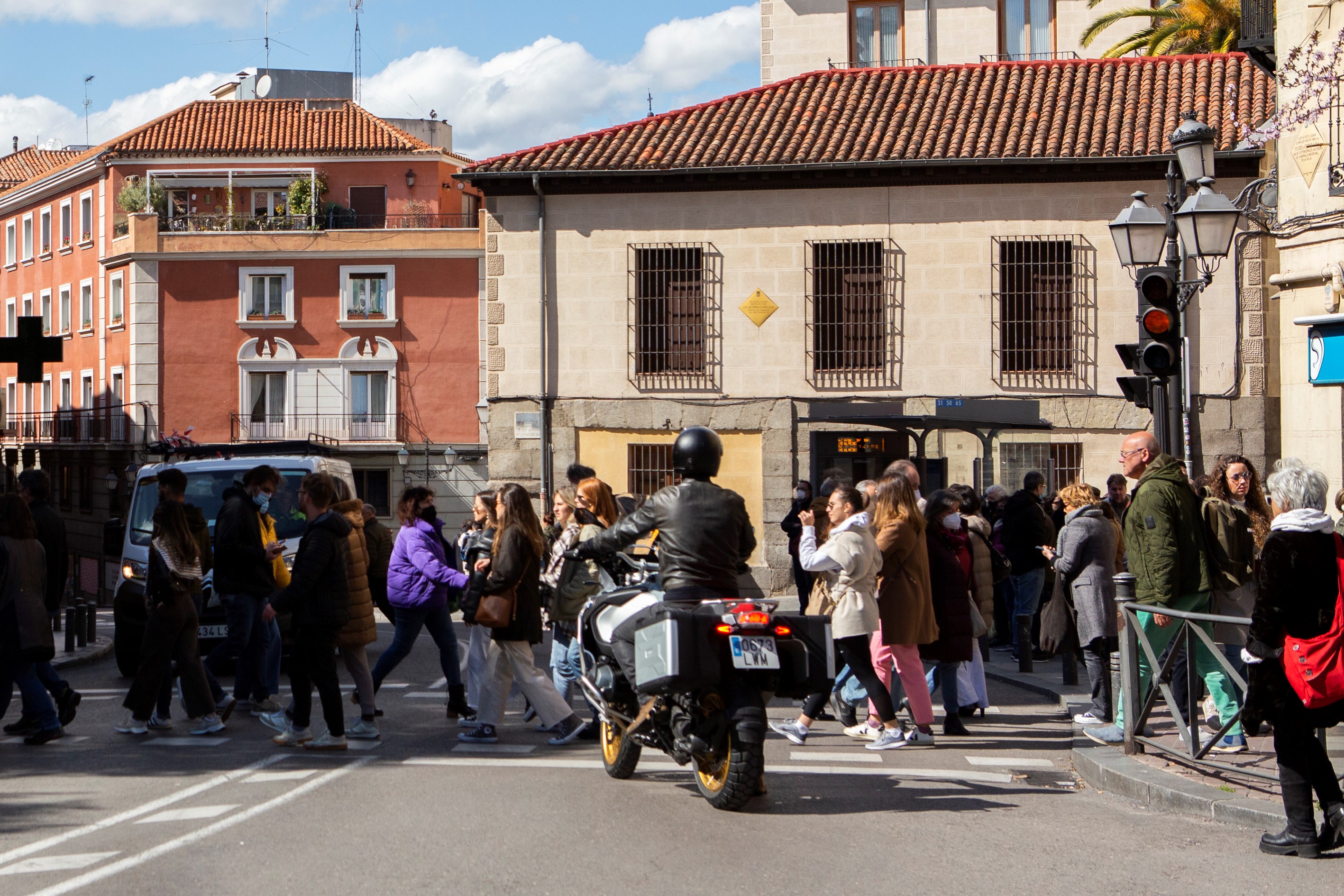 Imagen de una calle urbana con transeúntes cruzando un paso de peatones y una motocicleta parada delante.