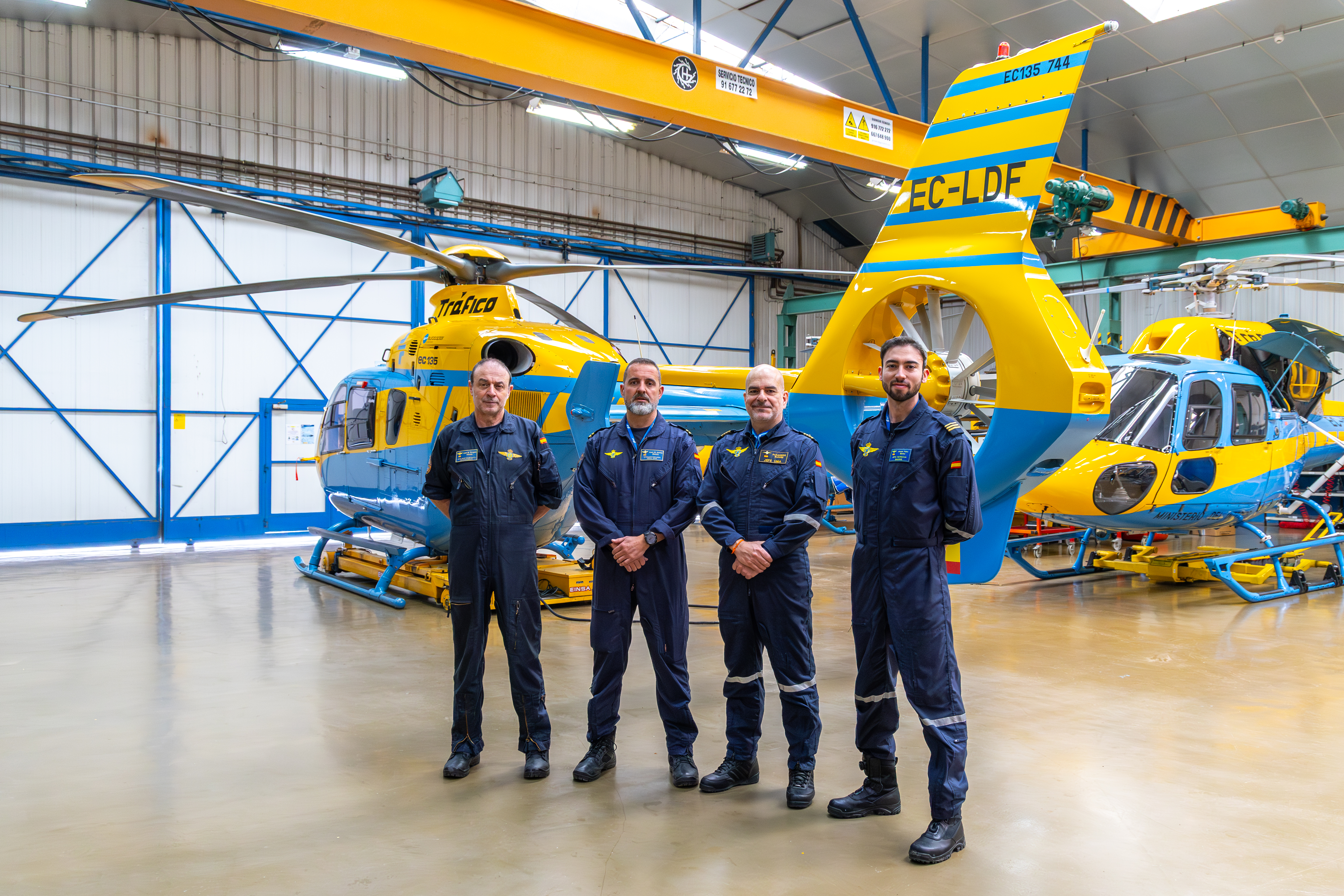 Cuatro hombres de posando uniformados con el traje de la UMA en un hangar con un helicóptero de fondo. 