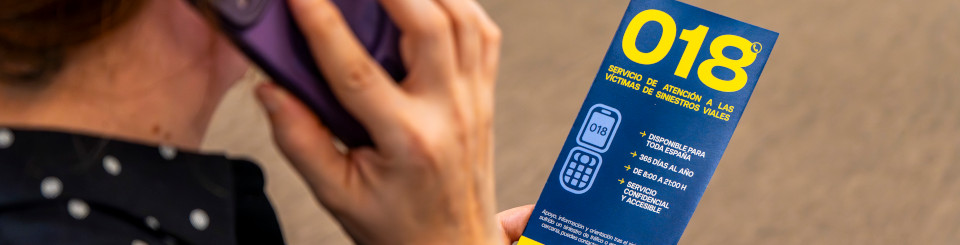 Mujer llamando por teléfono con un panfleto del servicio para víctimas de tráfico 018.