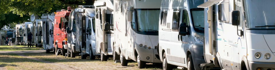 Autocaravanas estacionadas en fila junto a una zona arbolada