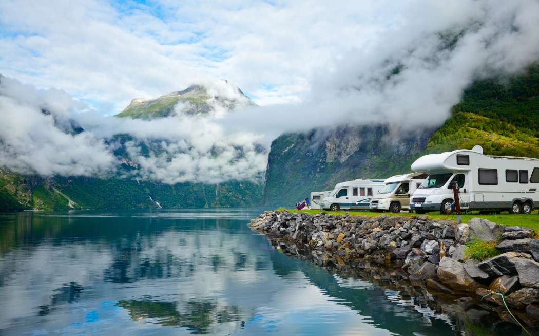 Autocaravanas aparcadas junto a un lago, con una montaña parcialmente cubierta por nubes al fondo