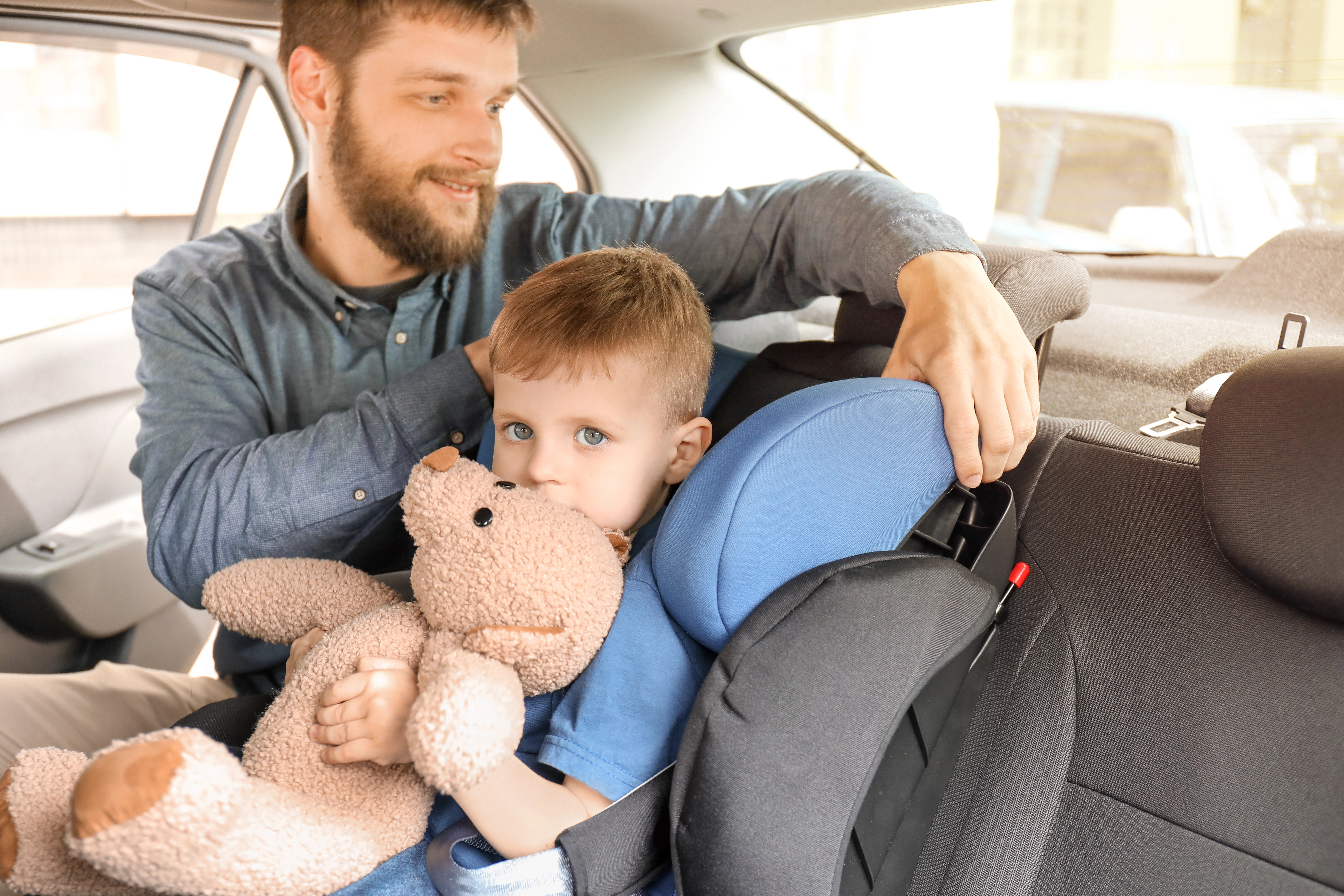 Hombre ajustando silla de niño dentro del coche con un niño sentado en ella.