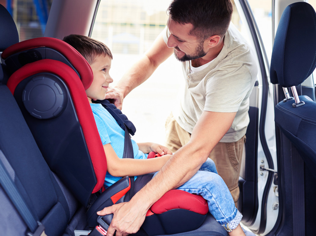 Un hombre en el interior de un coche ajustando la silla para niños con un niño sentado en ella.