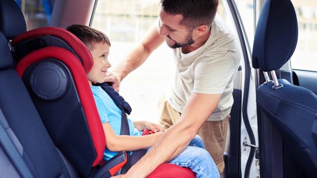Un hombre en el interior de un coche ajustando la silla para niños con un niño sentado en ella.