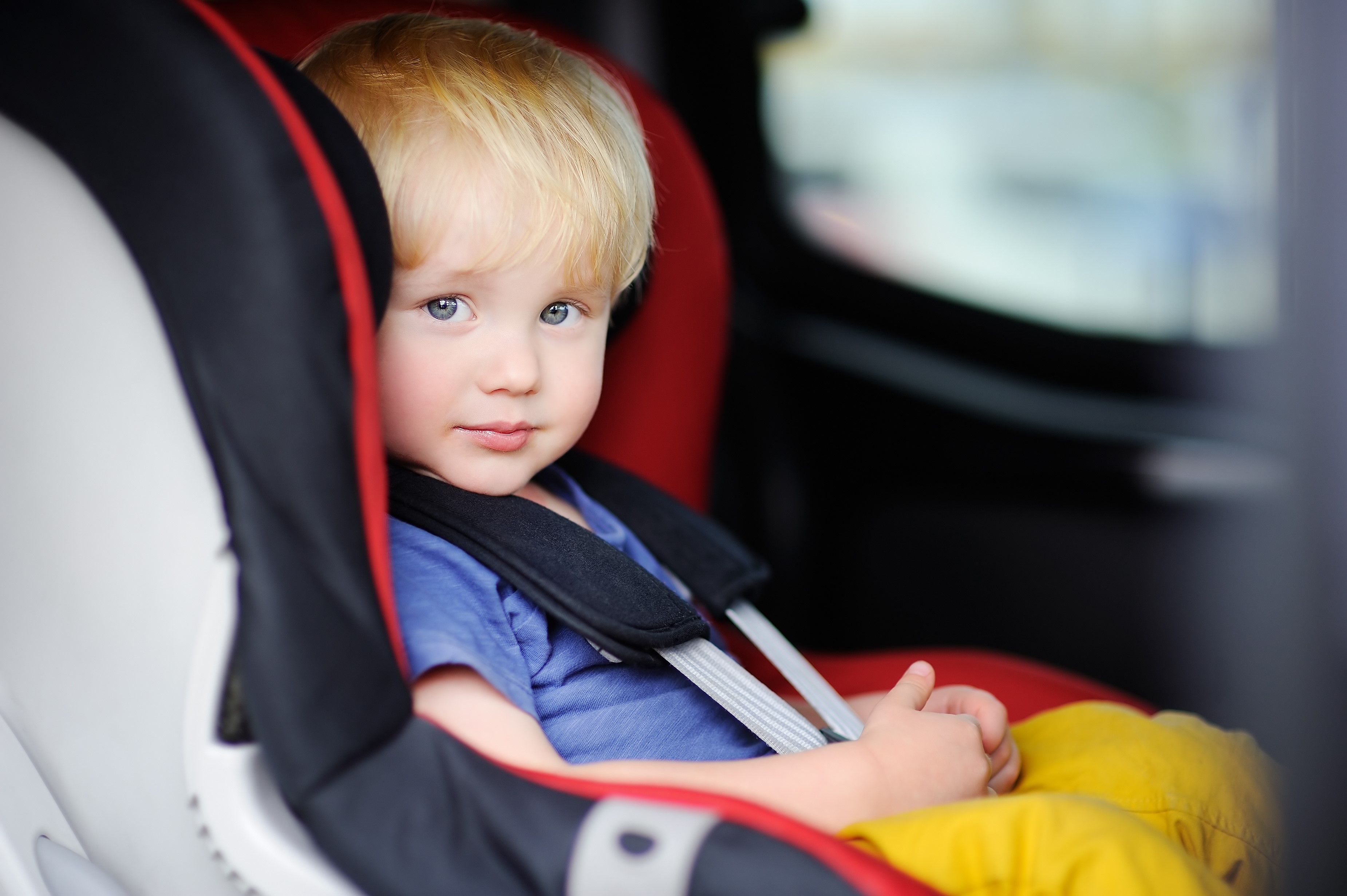 Niño de 1 o 2 años sonriendo y sentado en su sillita infantil en un coche.