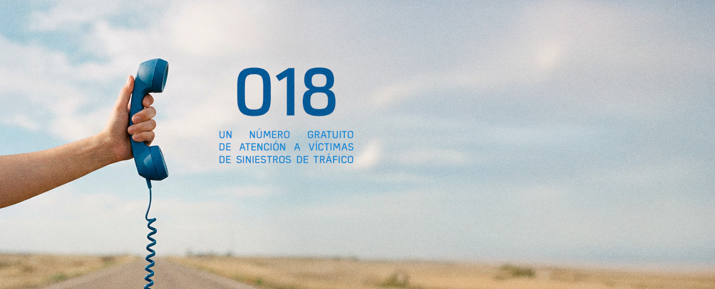 Imagen de una mano agarrando el auricular de un teléfono antiguo. A su lado se puede leer "018, un número gratuito de atención a víctimas de siniestros de tráfico". Como fondo de imagen hay una carretera de campo.