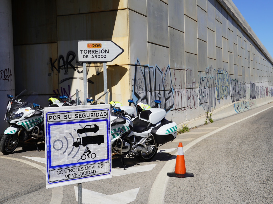Motos de la Guardia Civil en una carretera detrás de un cartel de control móvil de velocidad