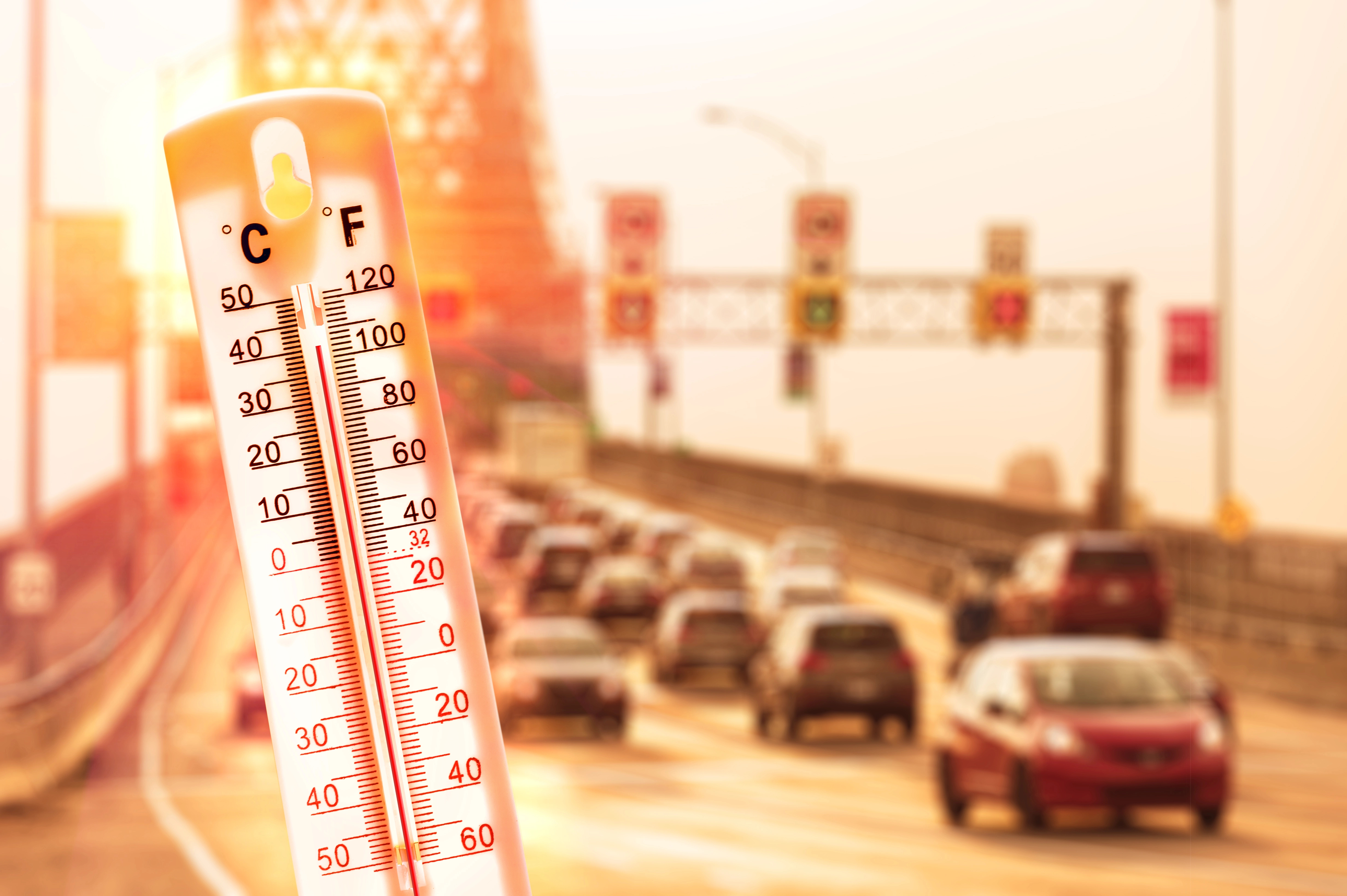 Termómetro marcando alta temperatura con carretera con coches de fondo